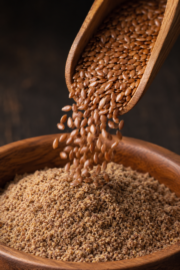 Whole flaxseeds pouring into cold-milled flax powder in a wooden bowl